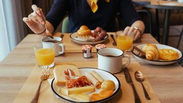 Une table mise pour le petit-déjeuner, avec une assiette de nourriture, un verre de jus d’orange et une tasse de café.
