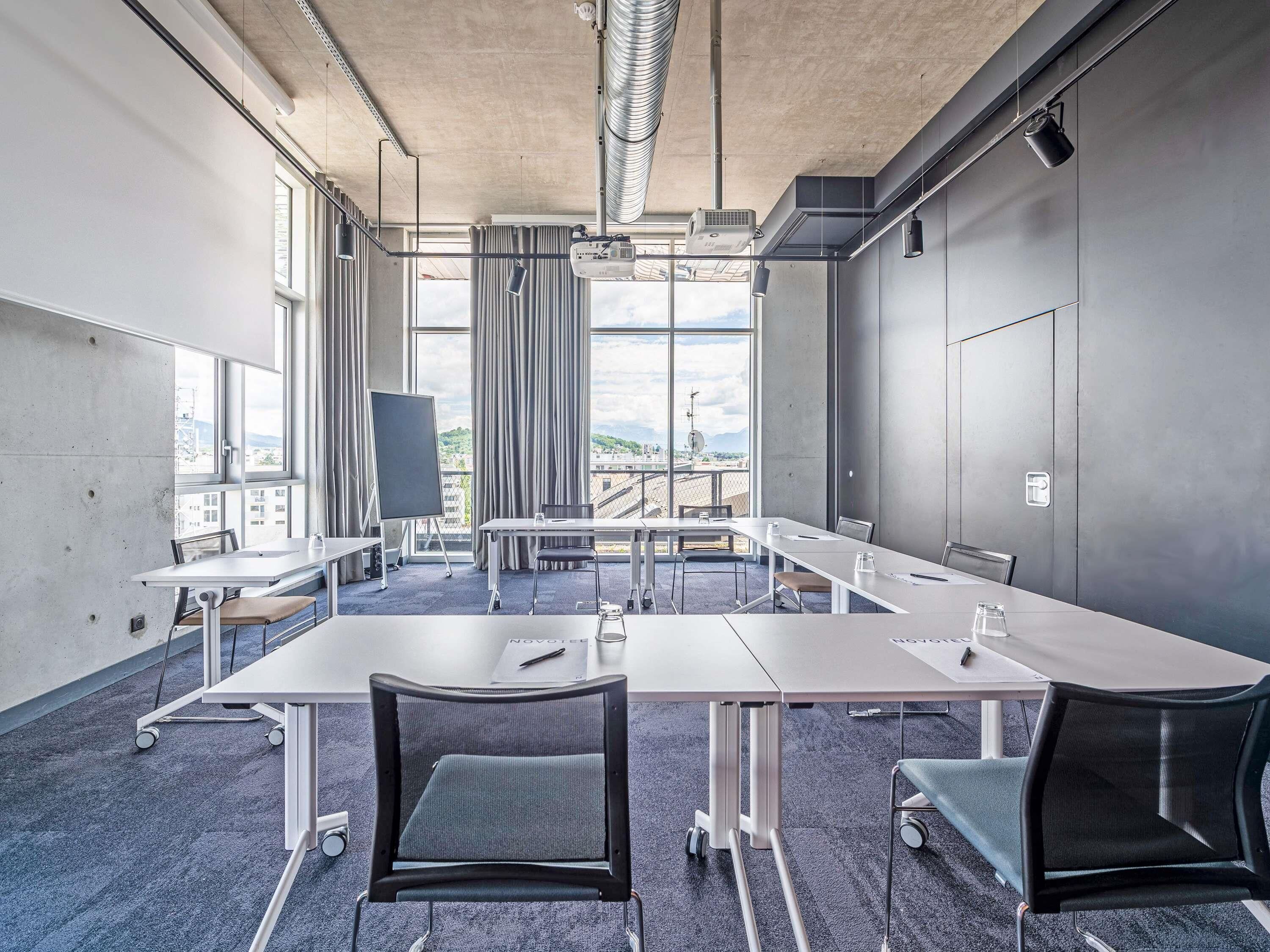 A conference room with a long table, chairs, a projector, and large windows with a city view.