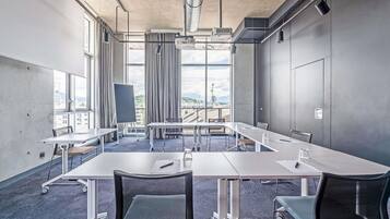 A conference room with a long table, chairs, a projector, and large windows with a city view.