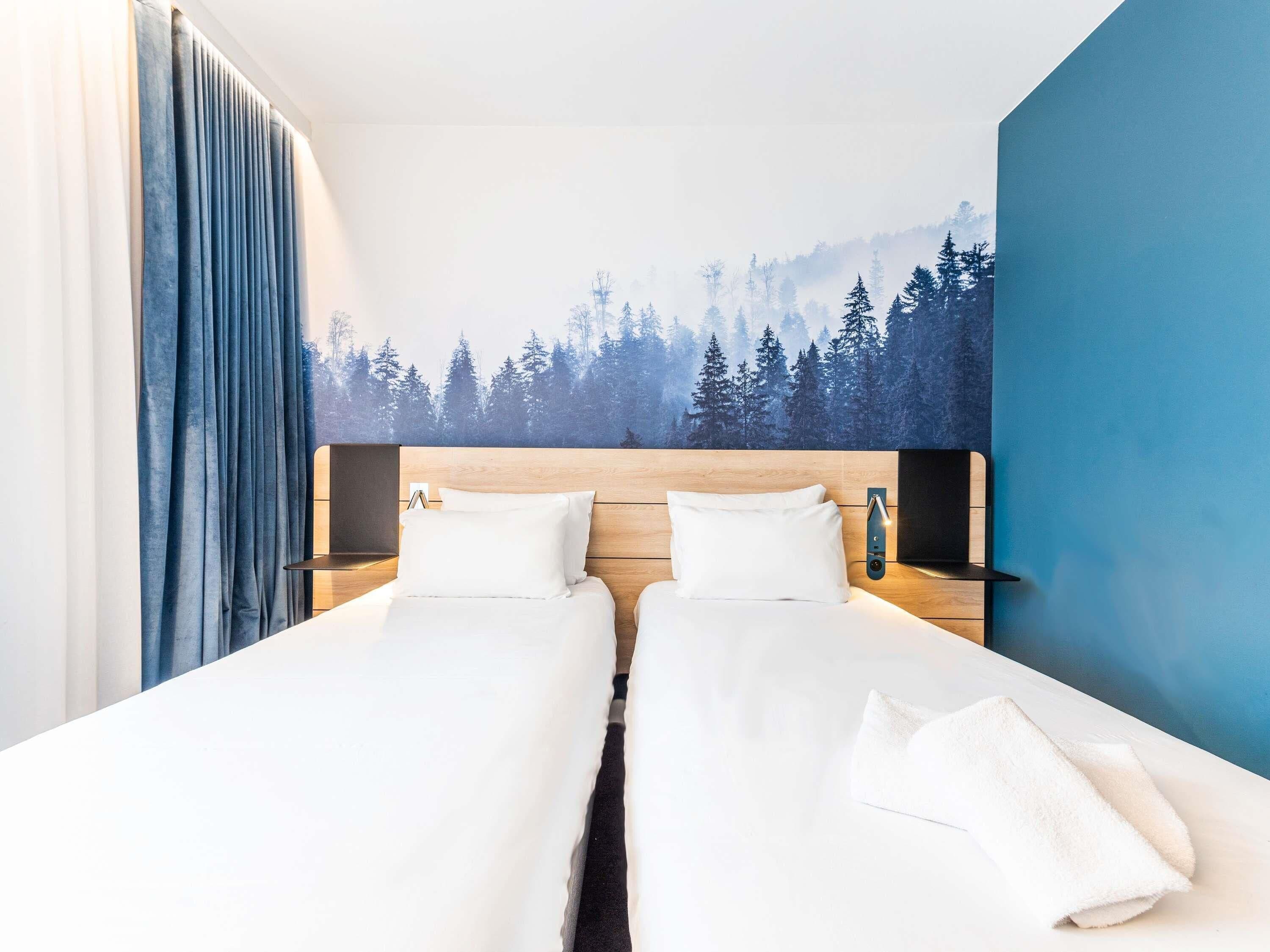 A double bed room with a forest mural, a bedside table, and a blue accent wall.