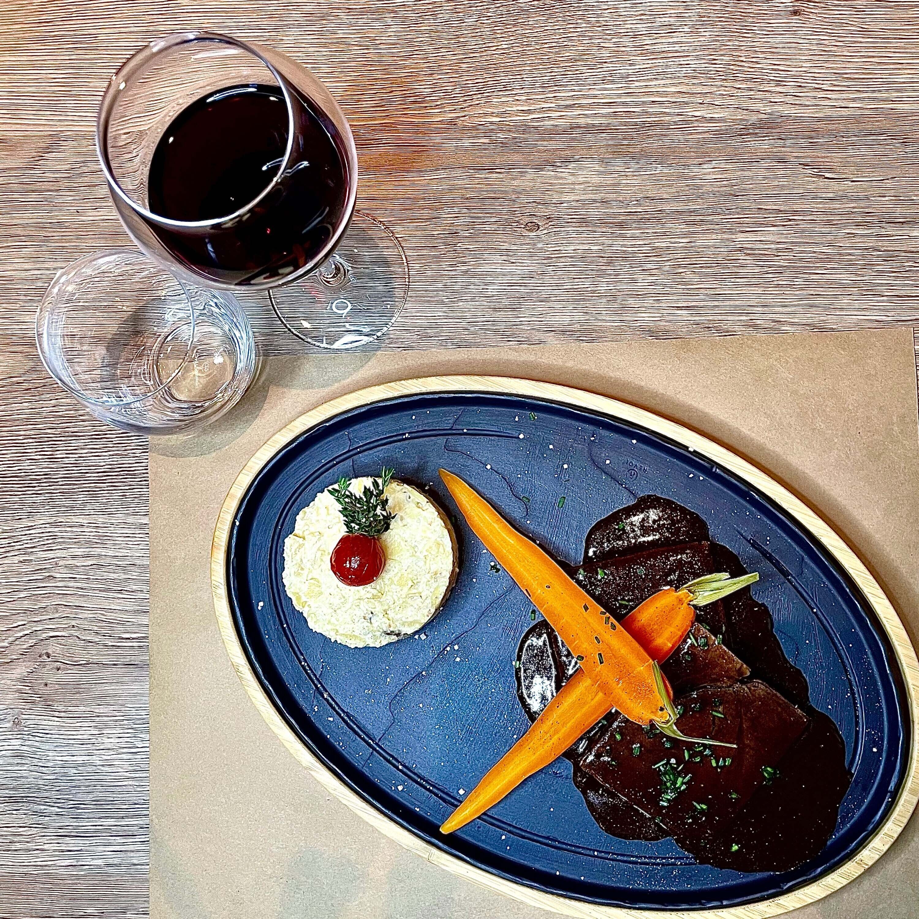 A blue plate with a dessert and a glass of red wine on a wooden table.