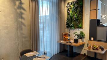A modern kitchen with a dining area, a large window with sheer curtains, and a wall-mounted plant.