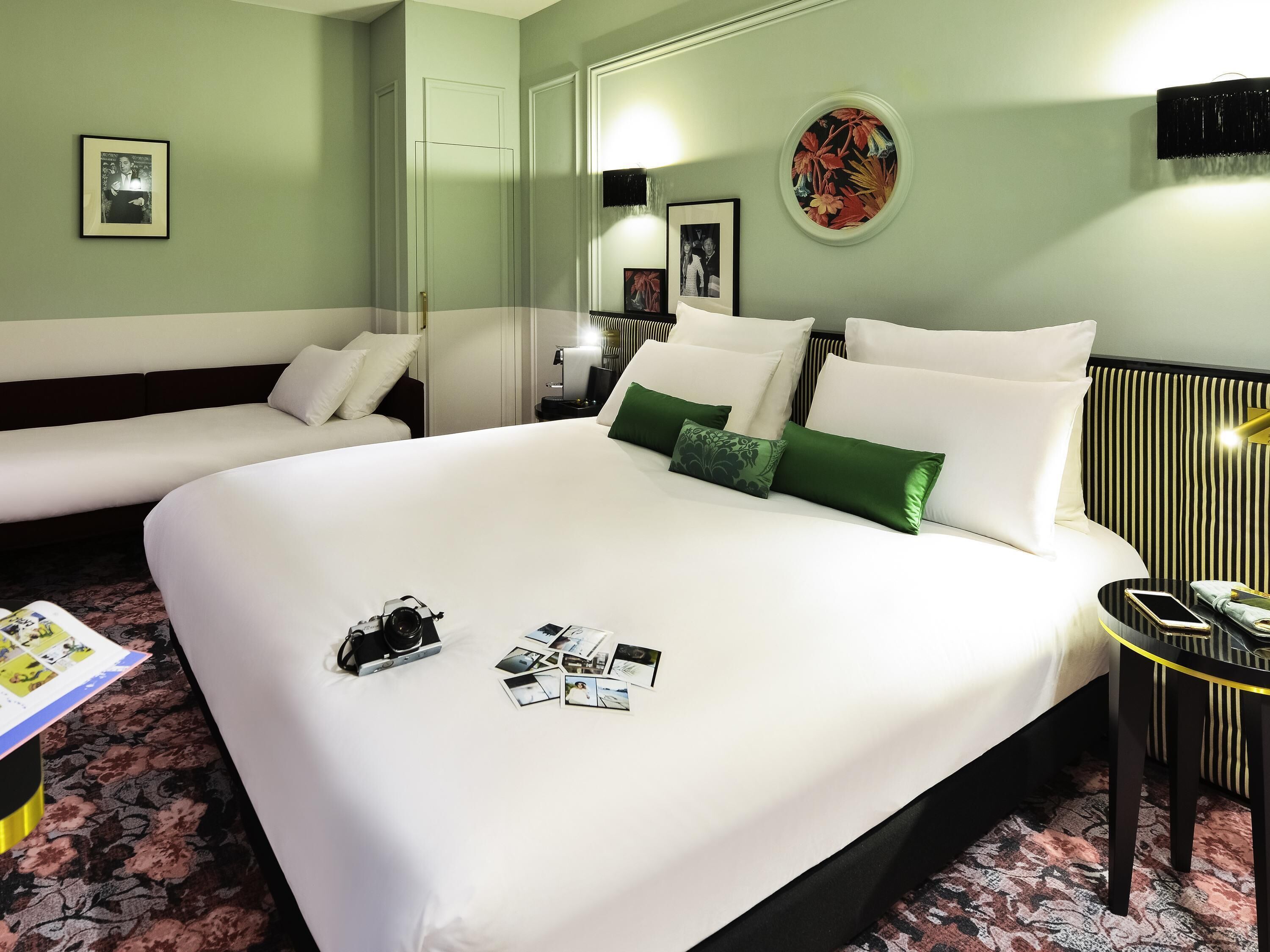 A hotel room with a large bed, two bedside tables, a sofa, and a mirror.