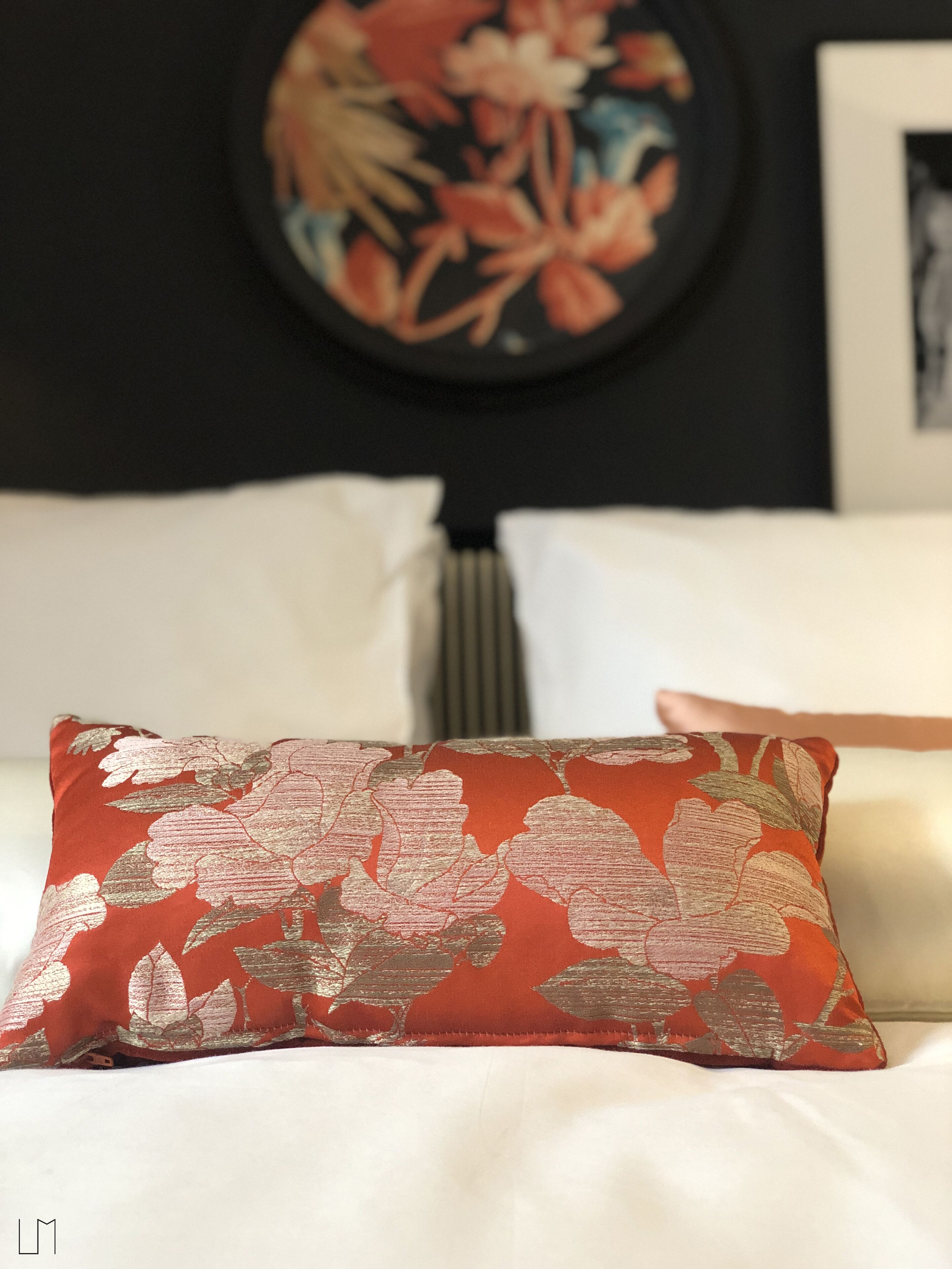 Una cama con un cojín estampado con motivos florales, una obra de arte enmarcada en la pared y un radiador.