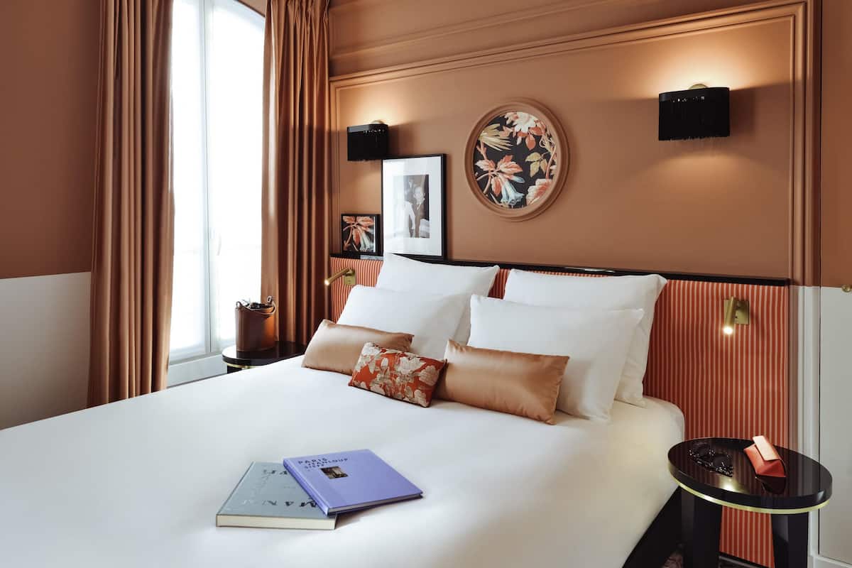 A hotel room with a large bed, a bedside table, a wall-mounted lamp, and a window with curtains.
