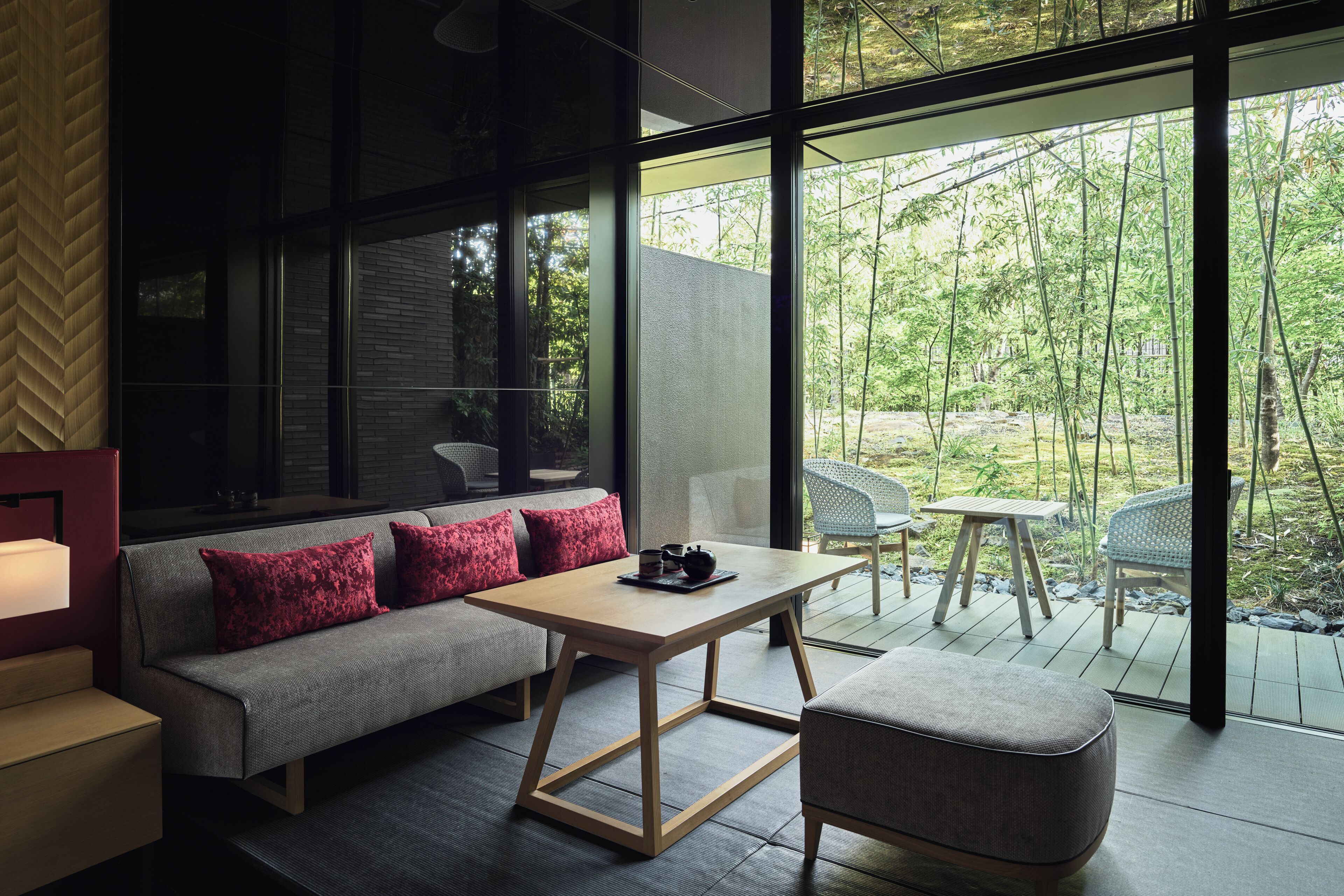 A modern interior with a sofa, a table, and a view of a bamboo forest through large windows.