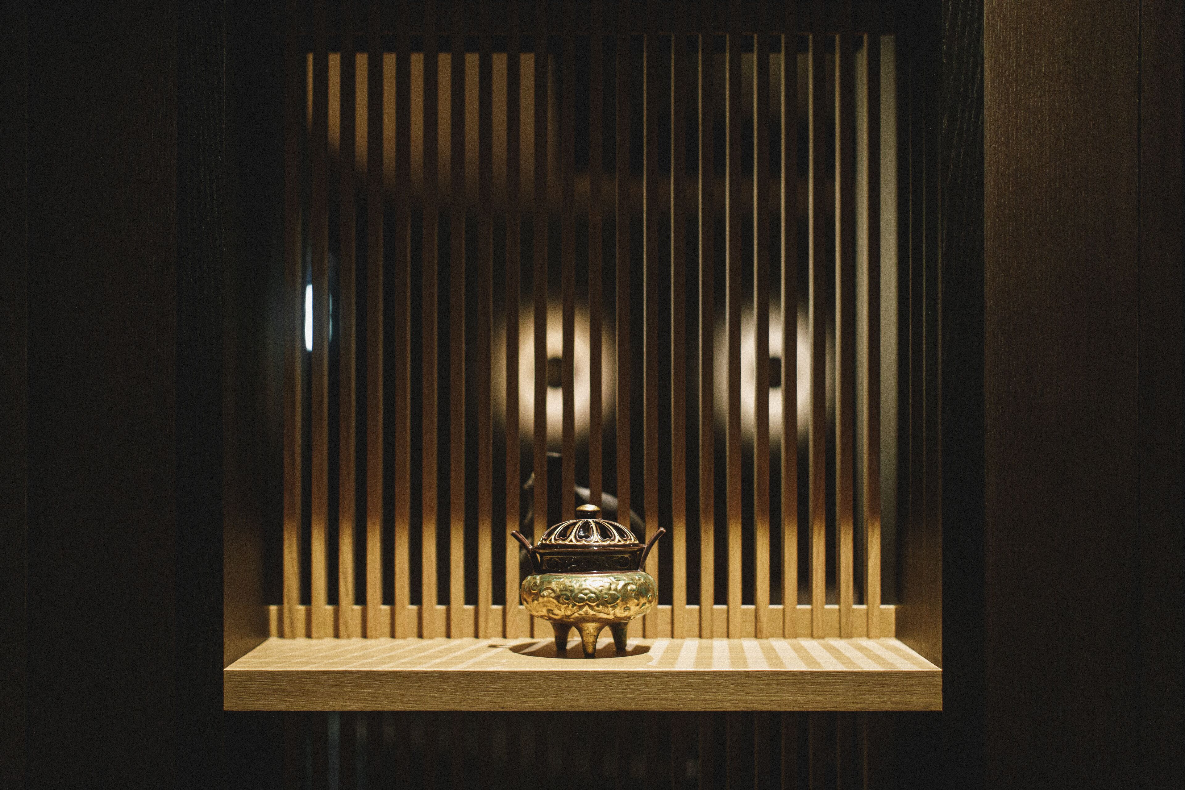 A traditional incense burner on a wooden shelf against a backdrop of vertical slats.