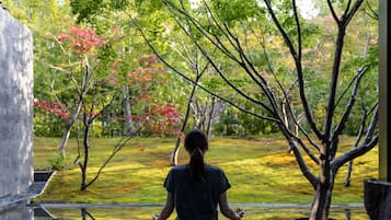 Una persona meditant en un entorn exterior tranquil, amb arbres i un estany.