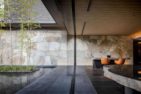 A modern interior with a stone wall, a reflective floor, and a seating area with two chairs. - Garrya Nijo Castle Kyoto (Kyoto)