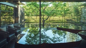 A modern interior with a large reflective water feature, a seating area with cushions, and a view of a lush garden through large windows. - Garrya Nijo Castle Kyoto (Kyoto)
