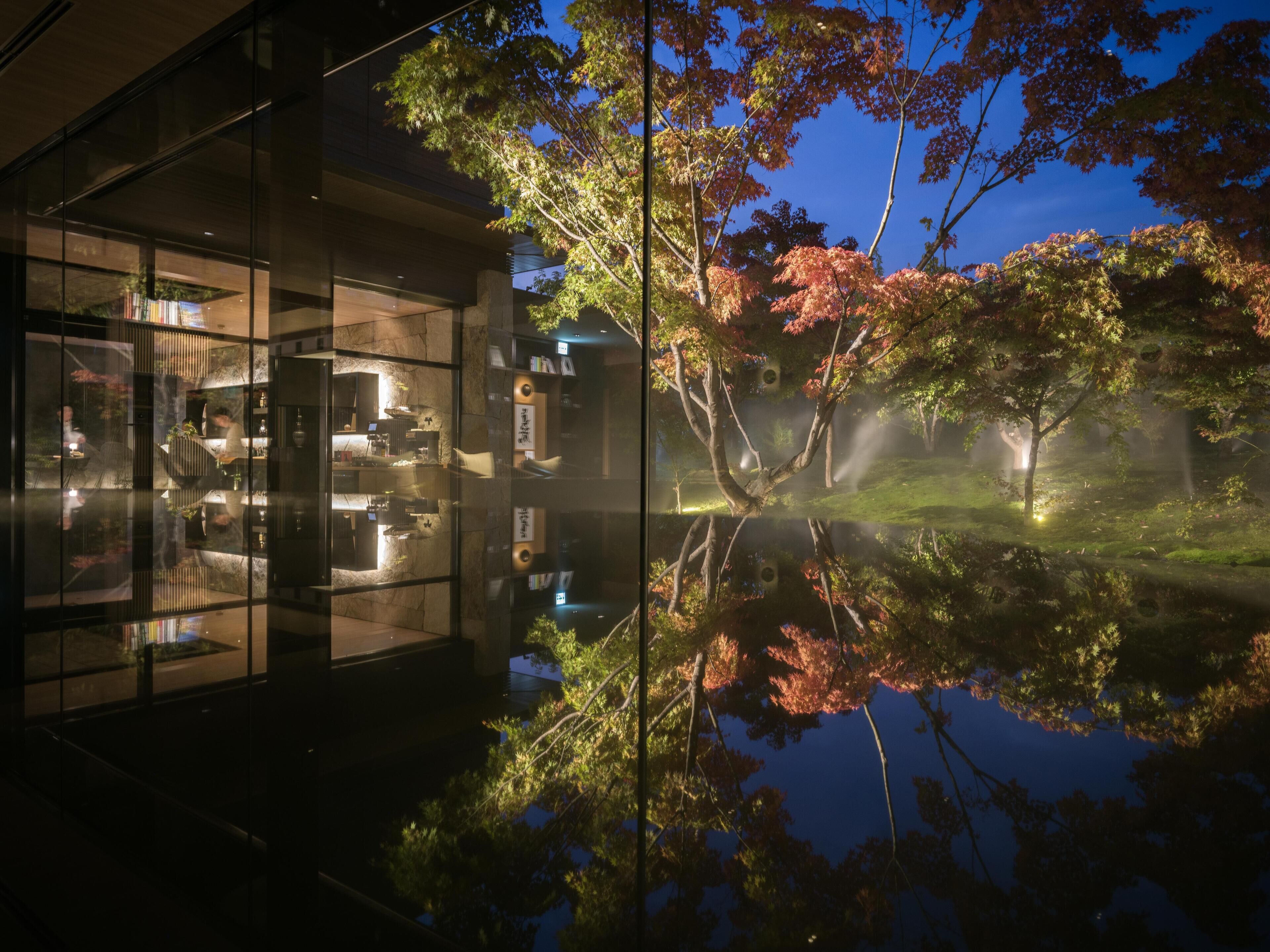 Un bâtiment moderne doté d’une façade en verre qui reflète les arbres et un étang.