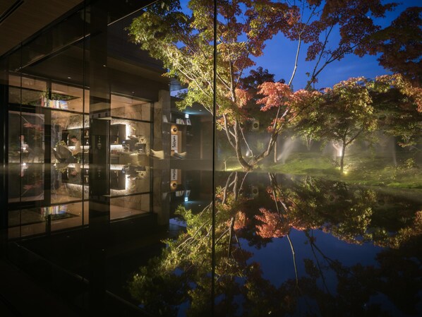 A modern building with a glass facade reflecting trees and a pond.