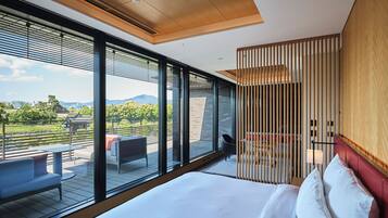 A modern hotel room with a large bed, a balcony with seating, and a view of the outdoors.