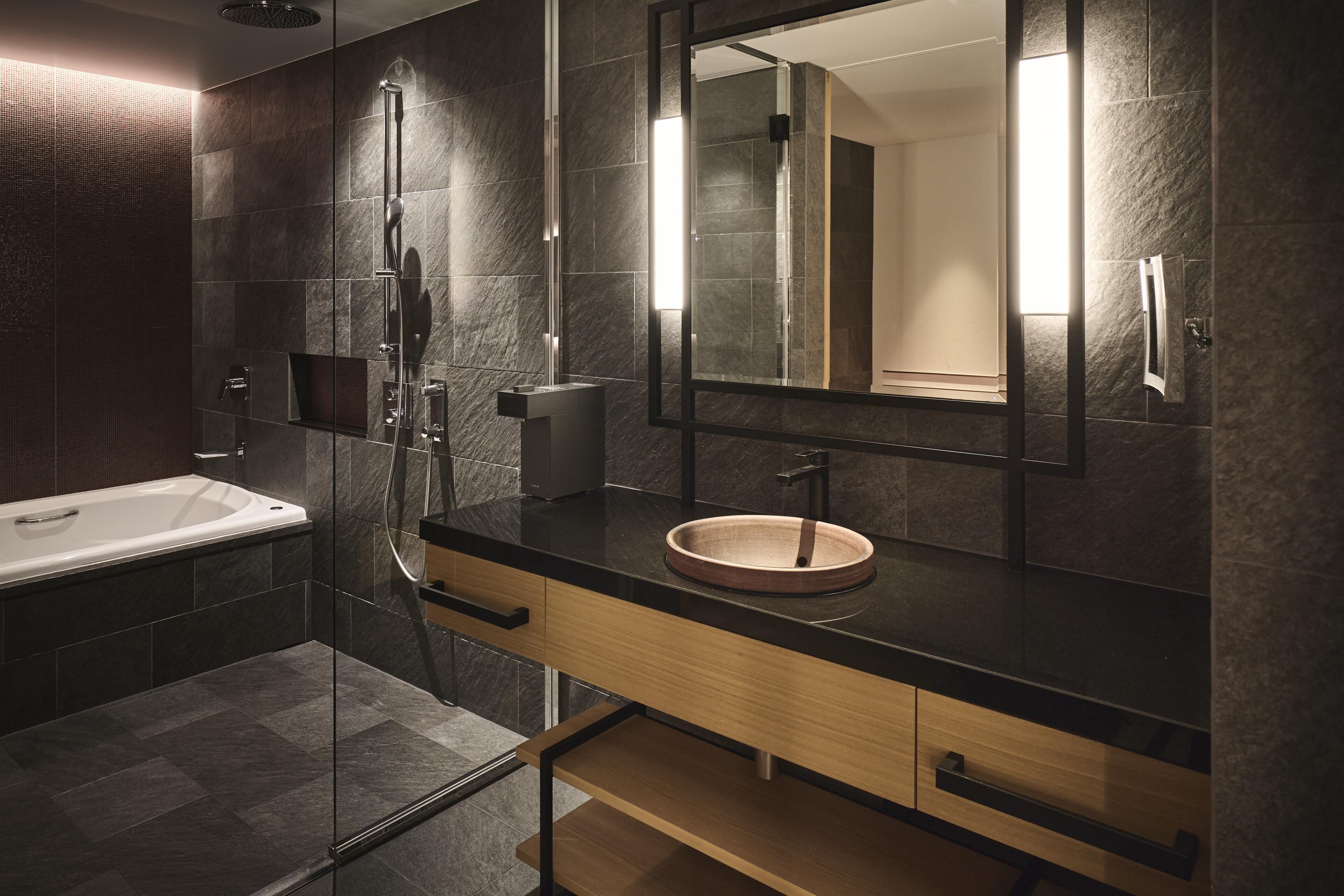 A modern bathroom with a bathtub, a round sink, a large mirror, and a glass-enclosed shower area.