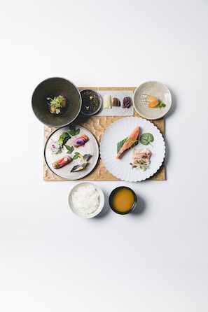 A variety of dishes including sushi, rice, and a bowl of soup, arranged on a wooden board.