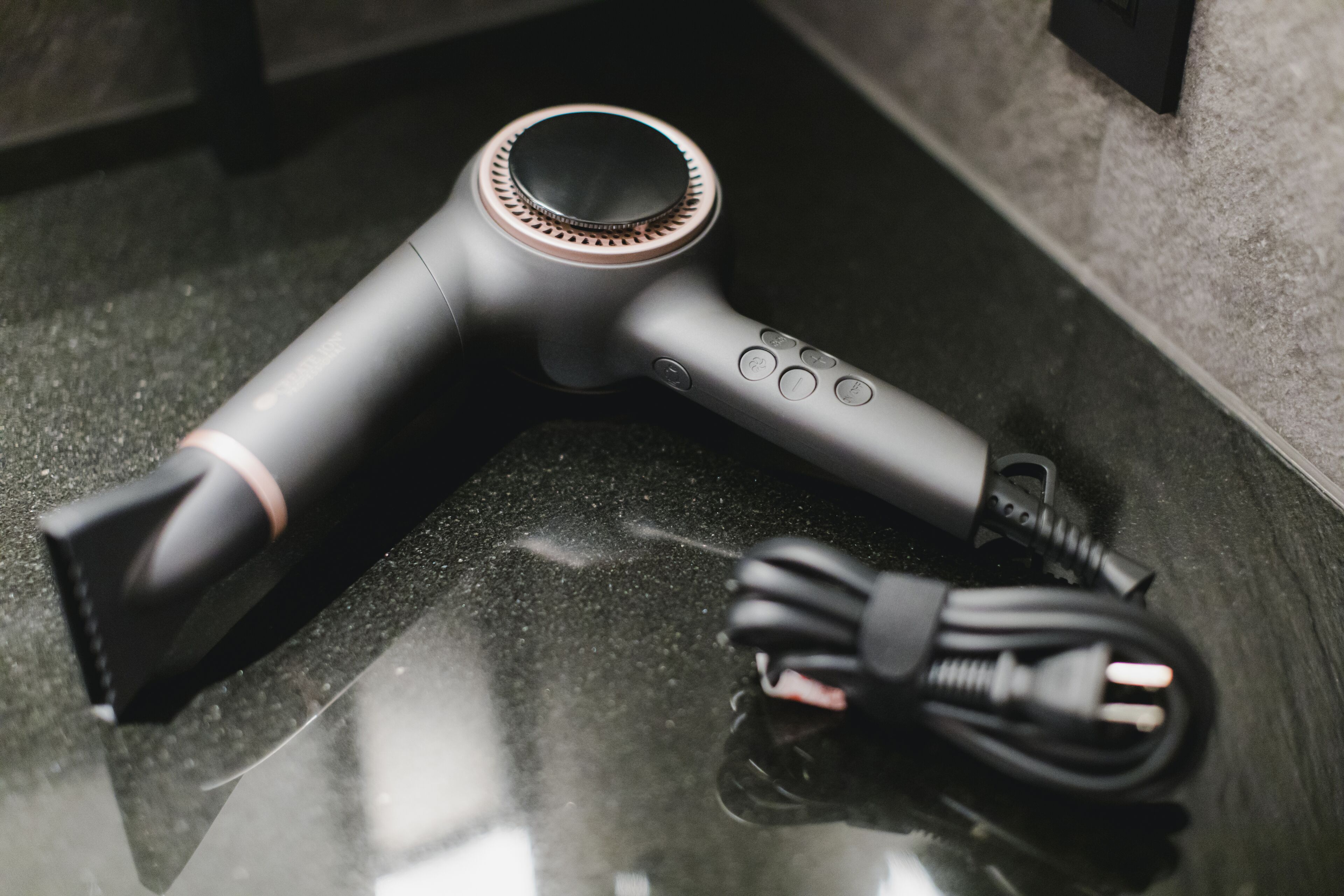 A hair dryer with a cord and a power adapter on a reflective surface.