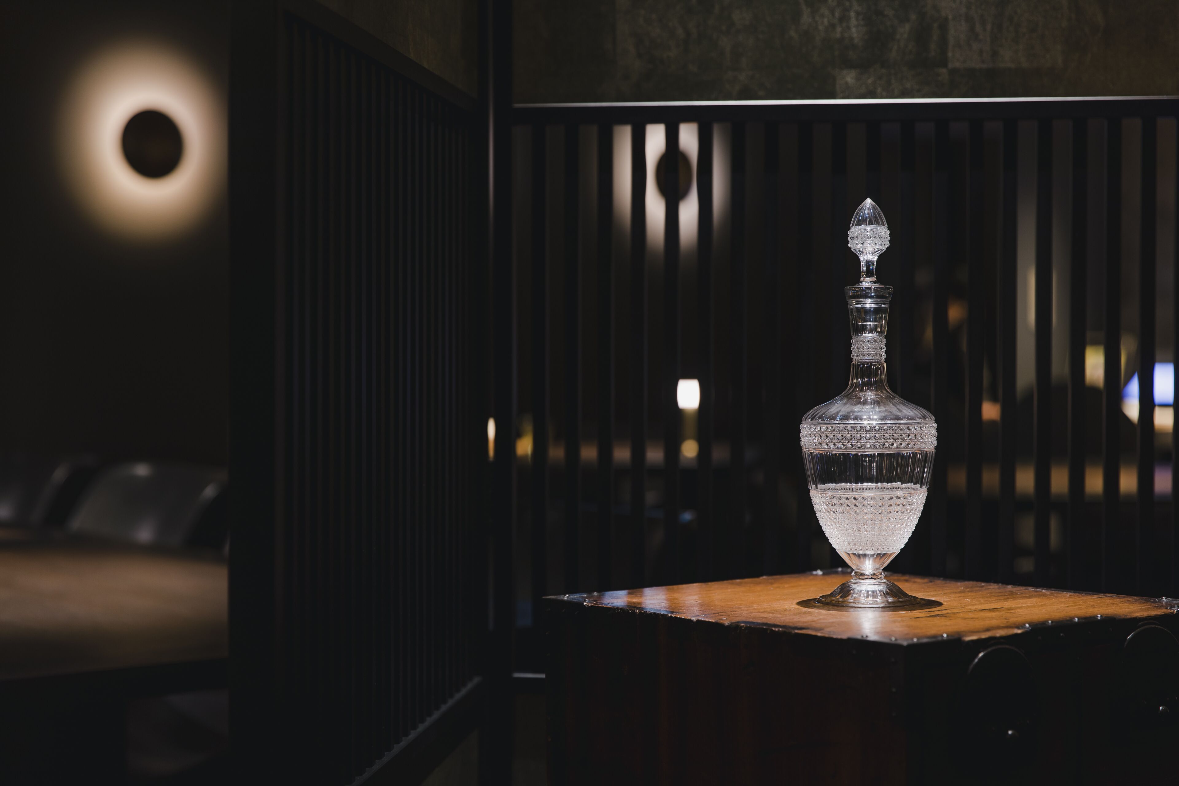 A dimly lit room with a wooden table and a crystal decanter.