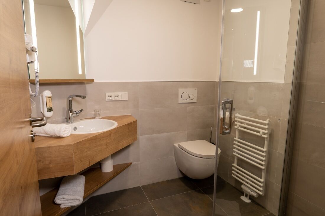 Un baño moderno con tocador de madera, lavamanos blanco, inodoro y cabina de ducha de vidrio.