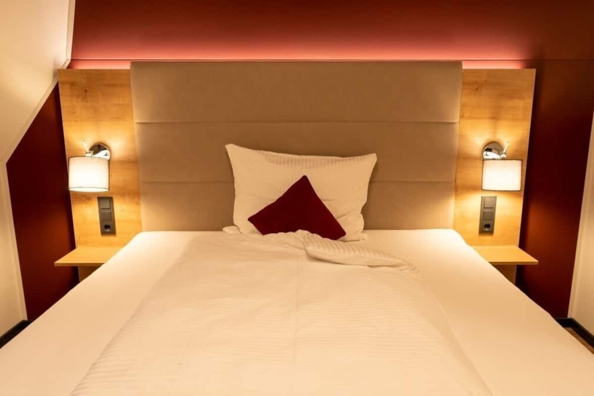Habitación de hotel con una cama grande, dos lámparas de noche y un cabecero de madera.