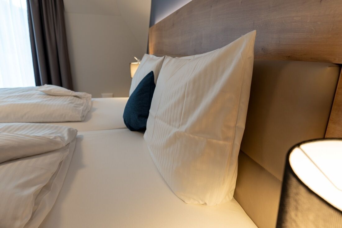 Una cama bien hecha con almohadas blancas y azul oscuro, un cabecero de madera y una lámpara de noche.