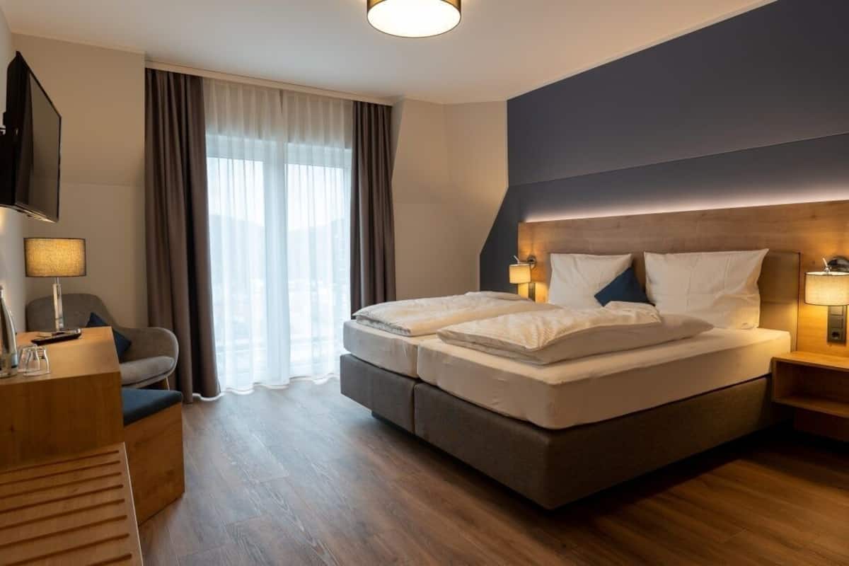 Una habitación de hotel con cama, lámparas de noche, televisor, escritorio y una silla.