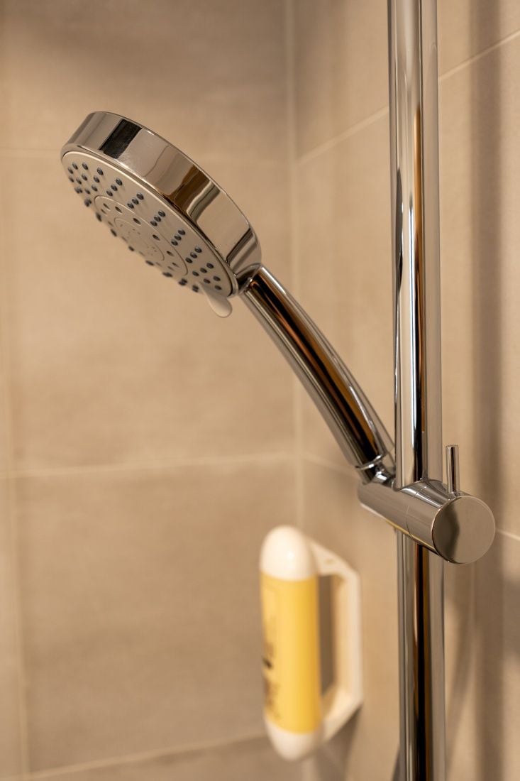 A chrome showerhead attached to a vertical pipe, likely part of a bathroom's plumbing system.