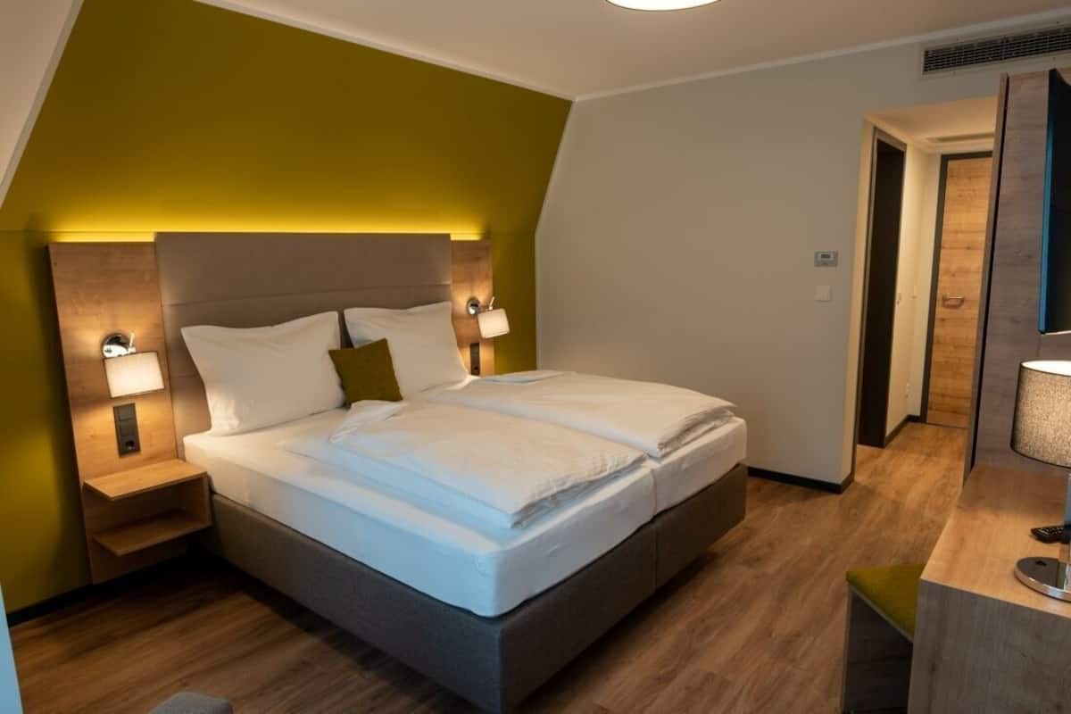 Una habitación de hotel moderna con cama, lámparas de noche, mesita de noche y suelo de madera.