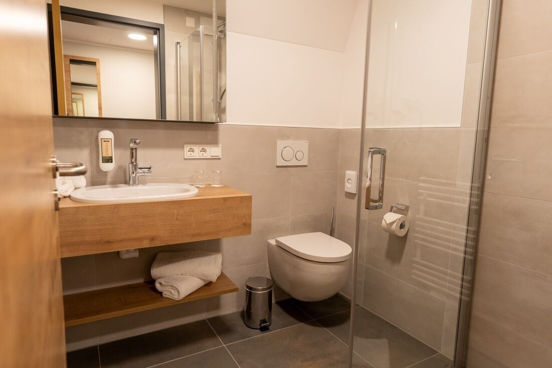 Ein modernes Badezimmer mit einem Holzlagerfläschchen, einem weißen Waschbecken, einer Toilette und einer Duschkabine aus Glas.