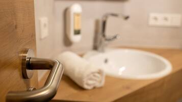 A bathroom with a wooden vanity, a white sink, a towel, and a hand dryer.