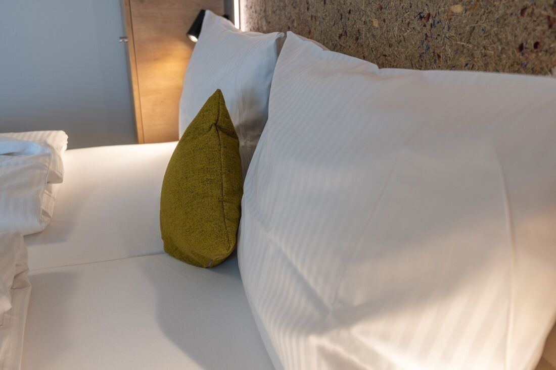 Ein Bett mit weißer Bettwäsche und einem einzelnen grünen Kopfkissen.