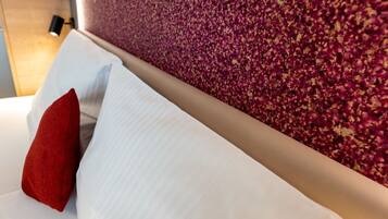 Cama com almofadas brancas e vermelhas, cabeceira de madeira e parede texturizada com padrão floral.