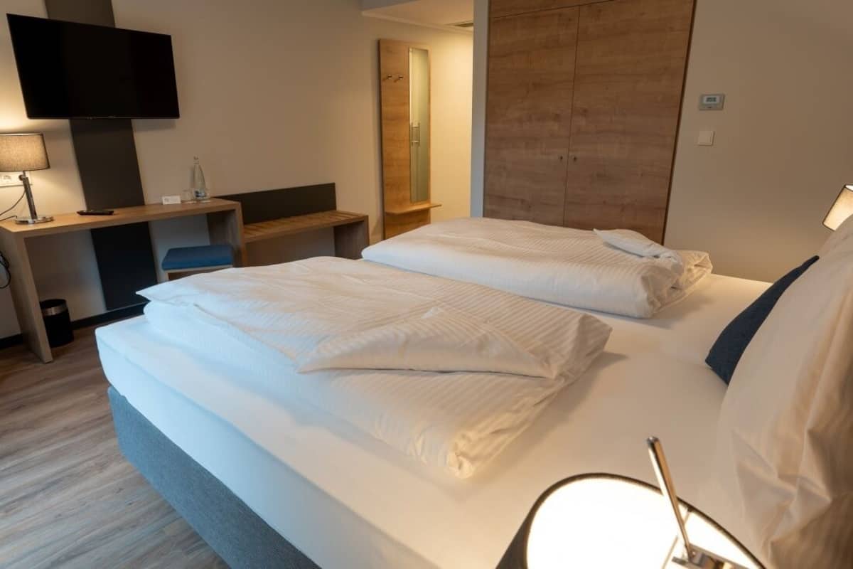 Una habitación de hotel con cama, escritorio, televisor y espejo.