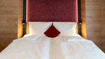 Un lit bien fait, avec du linge de lit blanc et un coussin rouge qui apporte une touche de couleur, le tout placé devant une tête de lit en bois agrémentée d’un panneau rouge texturé.