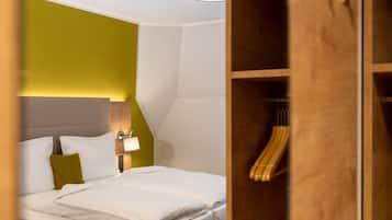 A modern hotel room with a neatly made bed, a wooden wardrobe, and a wall-mounted light fixture.
