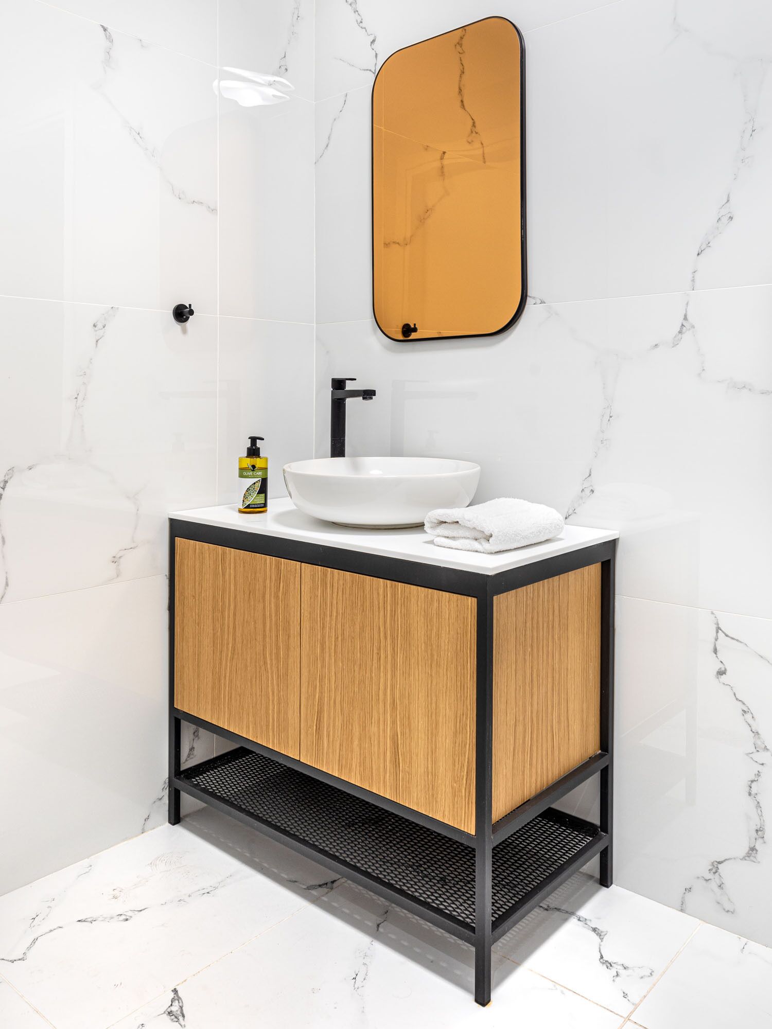 Bagno con lavabo in marmo bianco, mobile contenitore in legno e specchio con cornice di legno.