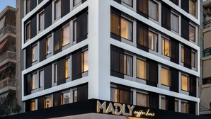 Een modern meerlaags gebouw met een platte gevel, grote ramen en een opvallend bord met de tekst 'MADLY coffee house' op de begane grond.