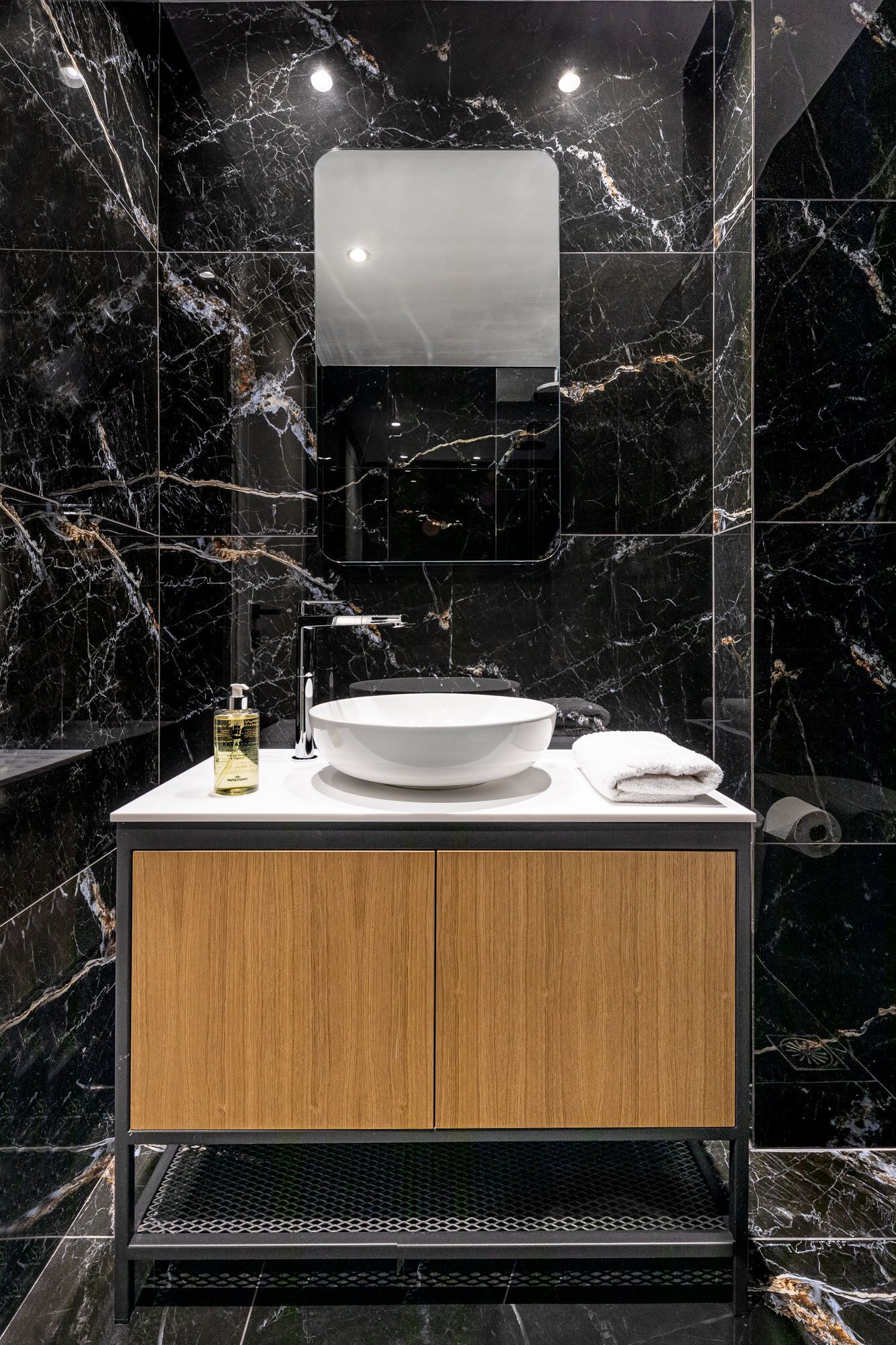 Un baño moderno con lavamanos de mármol, tocador de madera y un espejo grande.