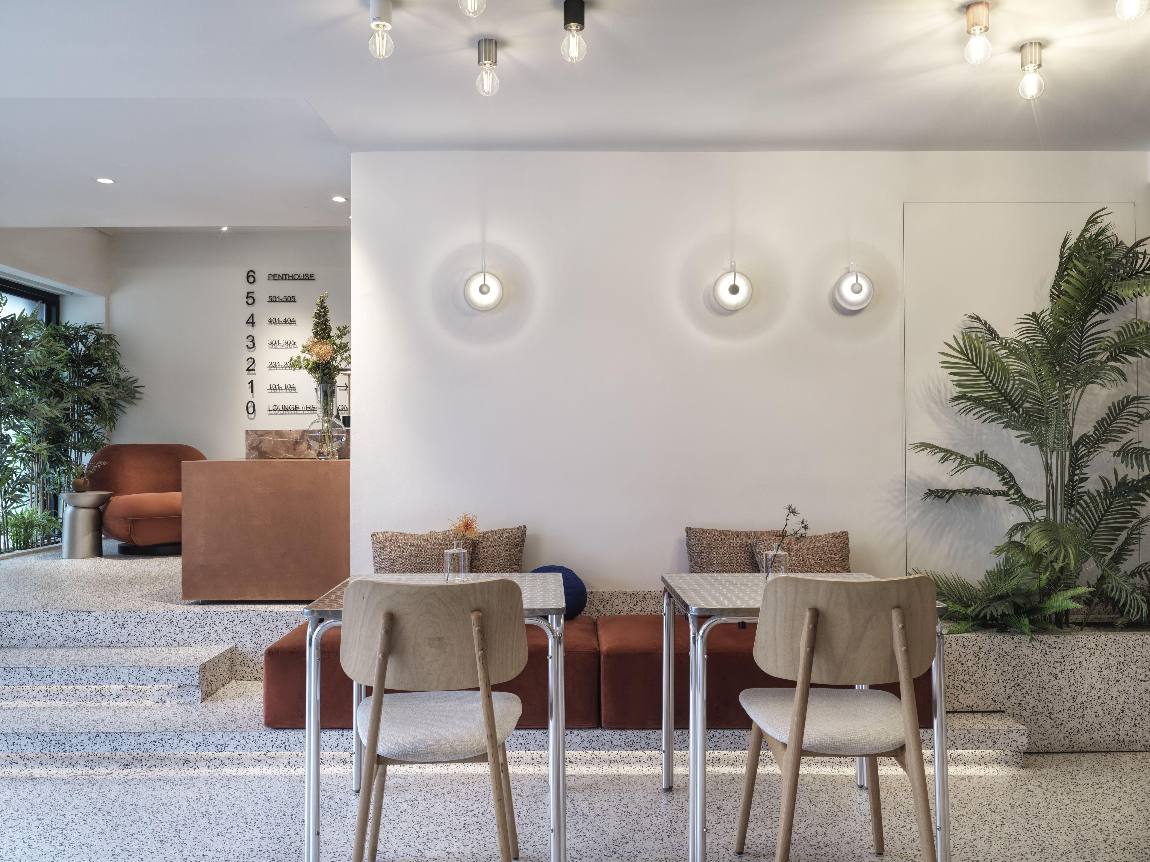 Een modern interieur met een eetgedeelte met twee tafels en stoelen, een zithoek met een bank en een wand met een overzicht.