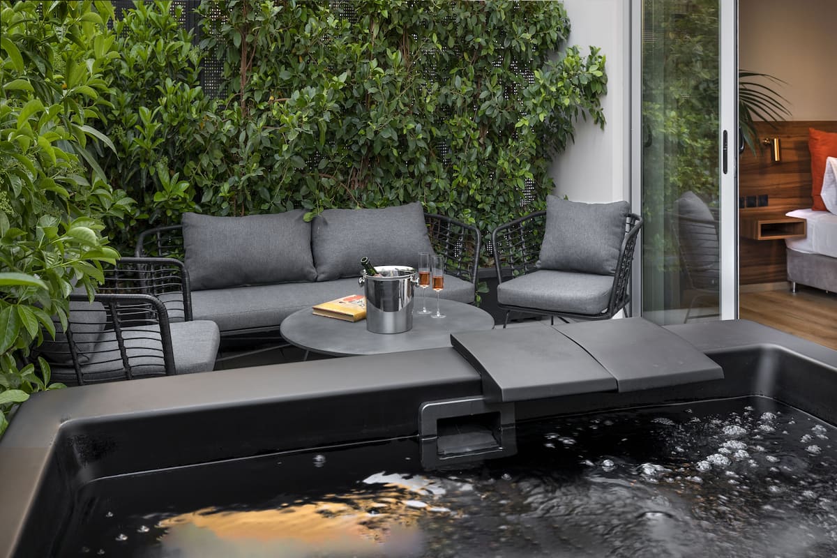 A modern outdoor seating area with a hot tub, surrounded by lush greenery and a glass partition.