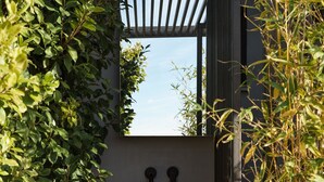 A modern outdoor bathroom with a stone basin, wooden table, and a pergola with climbing plants. - The Newel Acropolis (Athens)