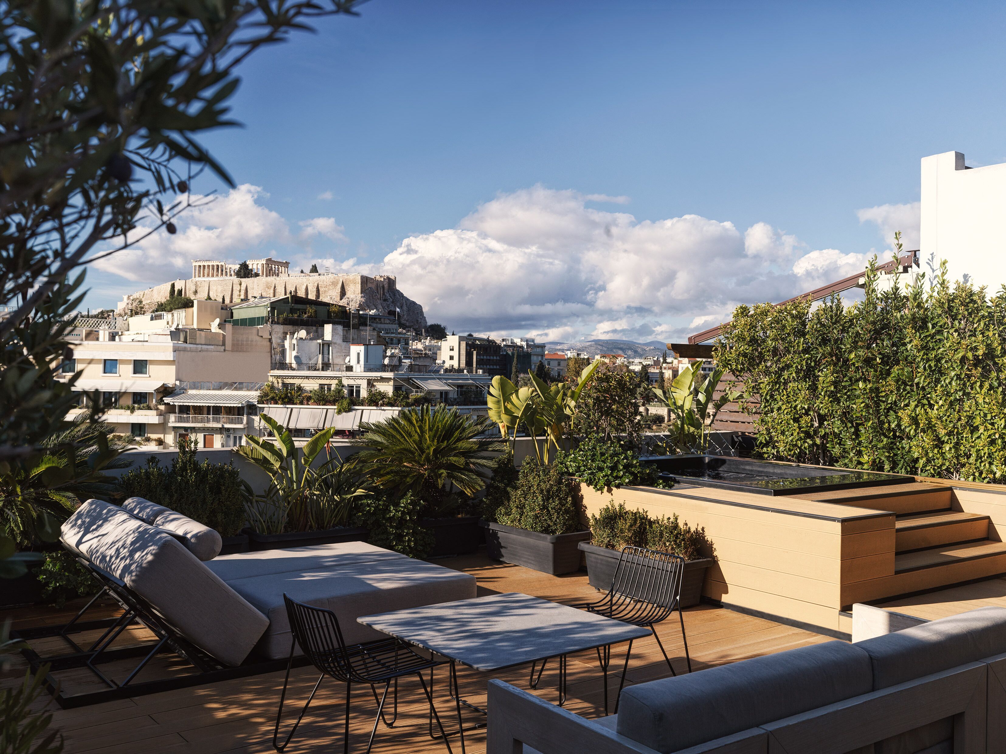 A rooftop terrace with outdoor seating, potted plants, and a view of the cityscape including a historic building.