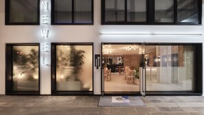 A modern building with large glass doors, a visible reception area, and a sign that reads "NEW". - The Newel Acropolis (Athens)