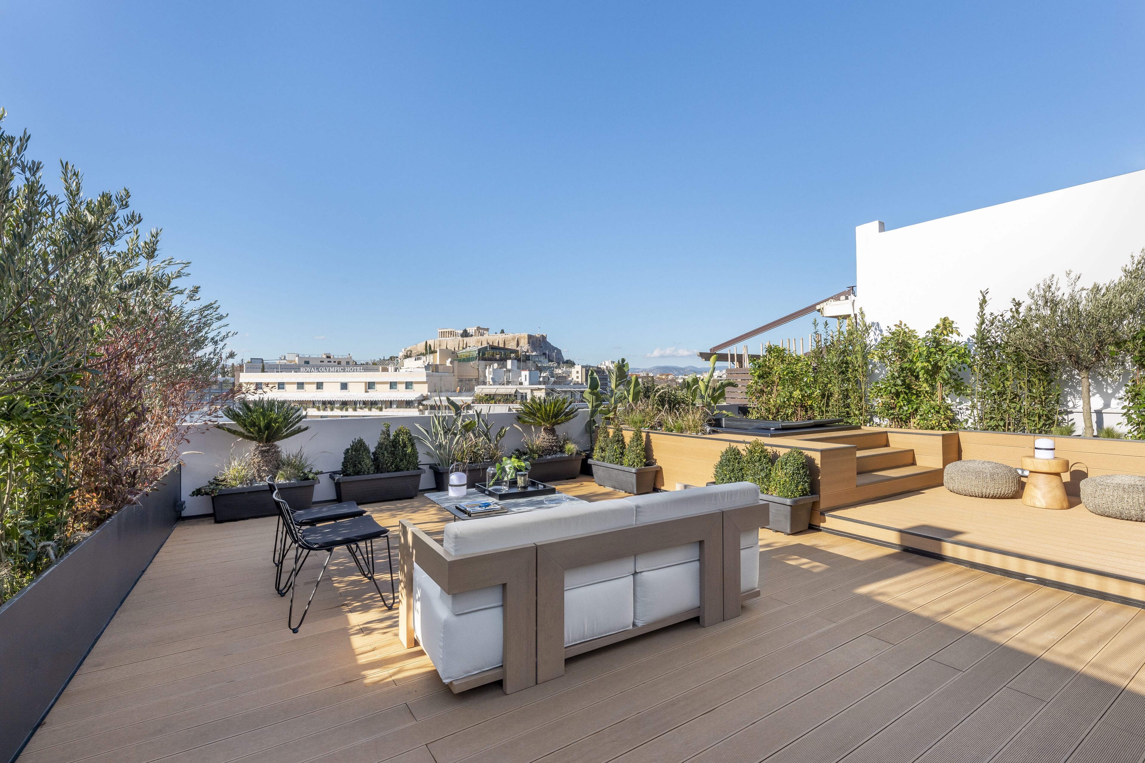 A rooftop terrace with a modern outdoor seating area, potted plants, and a view of a historic building in the background.