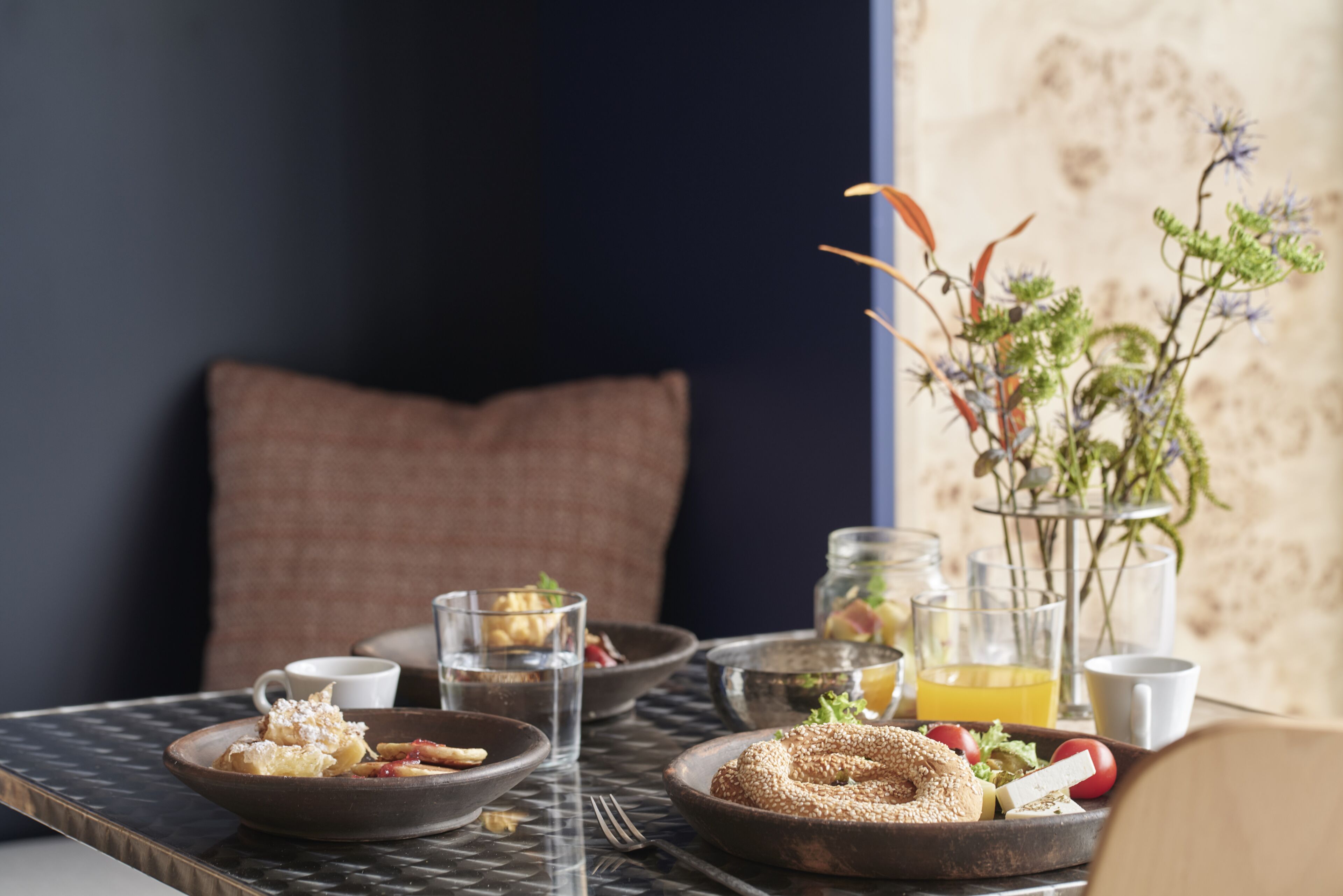 A breakfast setting with various dishes, glasses of water and orange juice, and a vase with flowers.