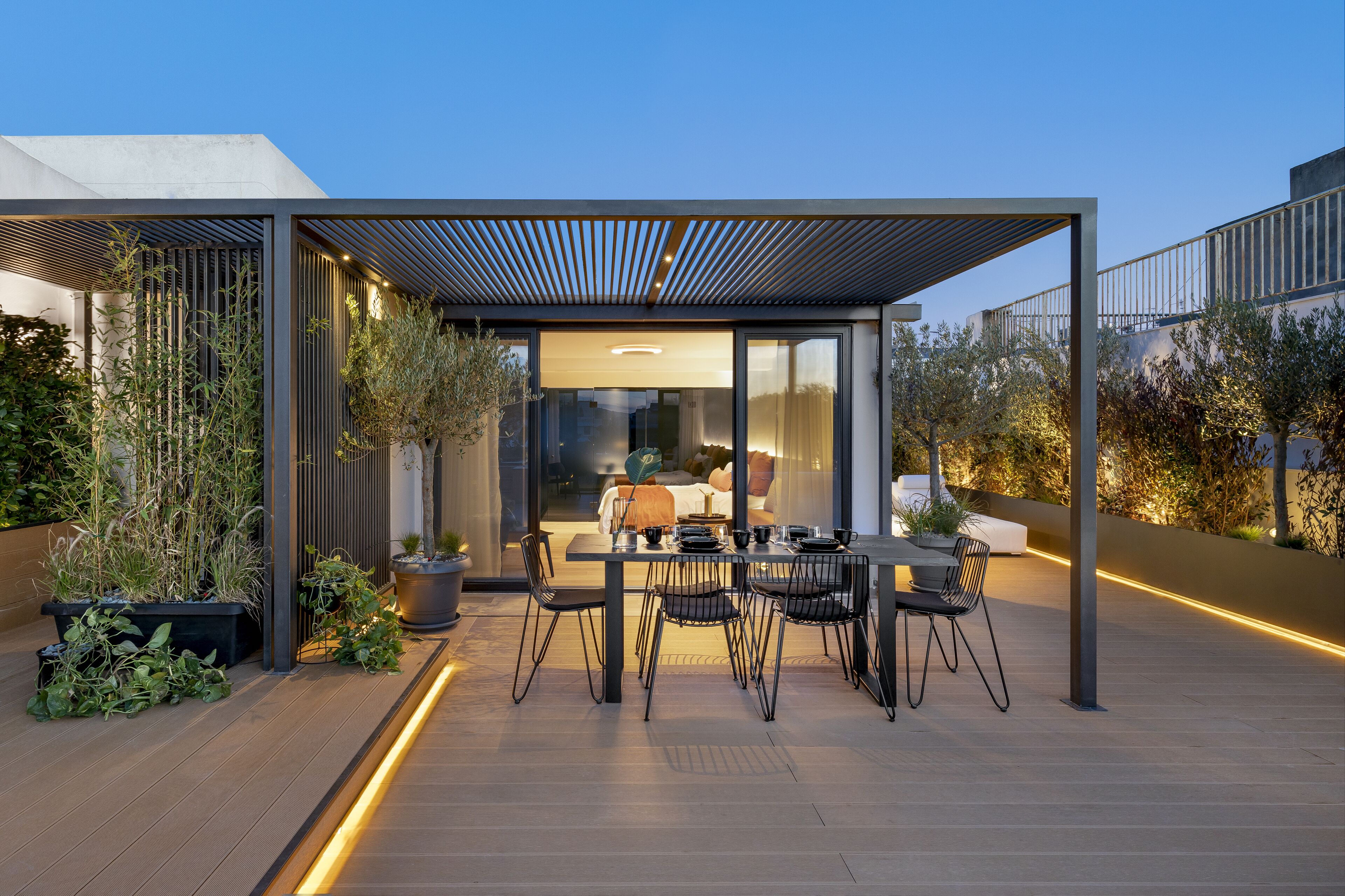 An outdoor dining area with a modern design, featuring a table and chairs, surrounded by potted plants and a pergola.