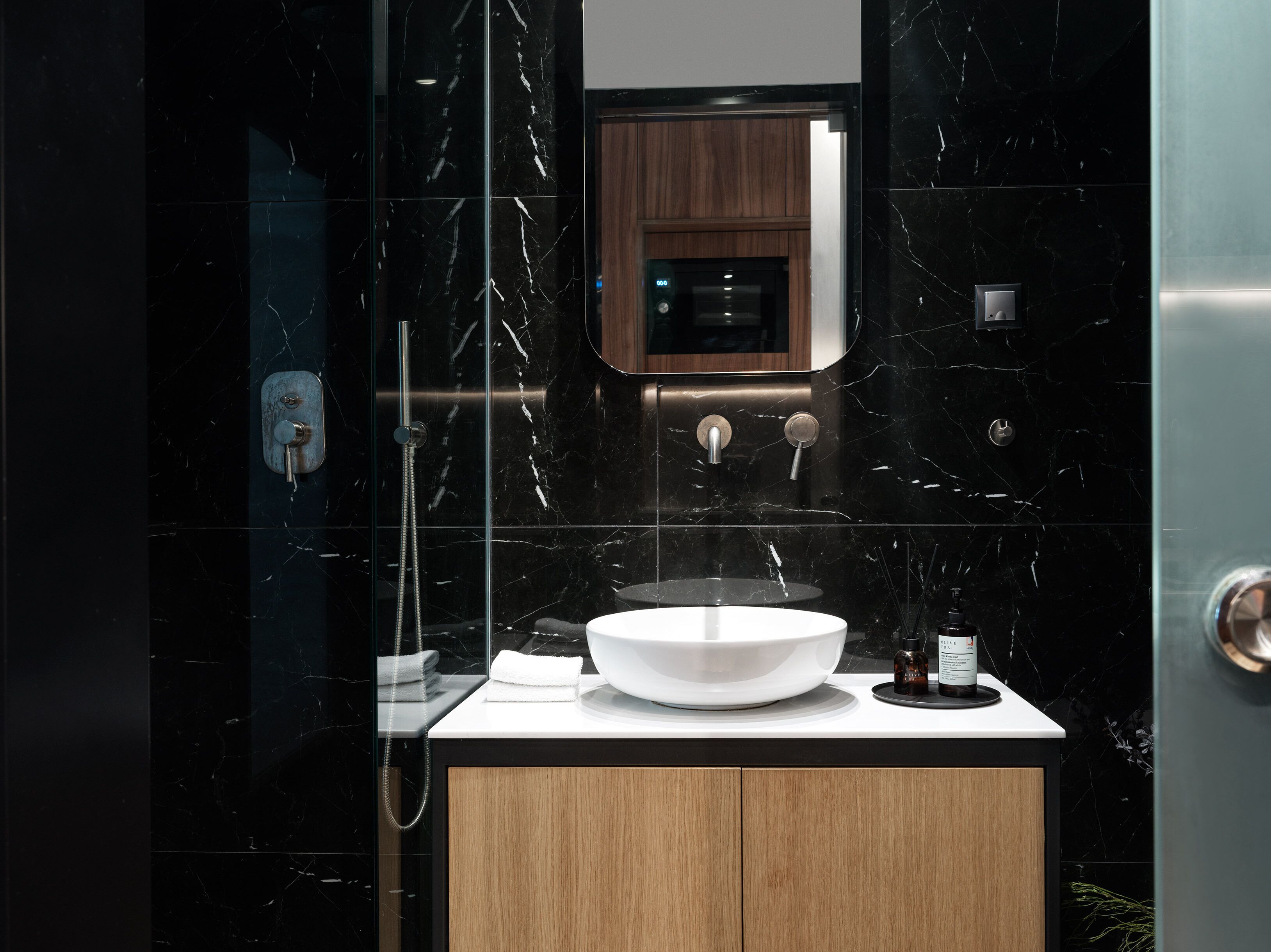 Ein modernes Badezimmer mit einem schwarzen Marmorwaschbecken, Holzschränken und einer Glaskabine für die Dusche.
