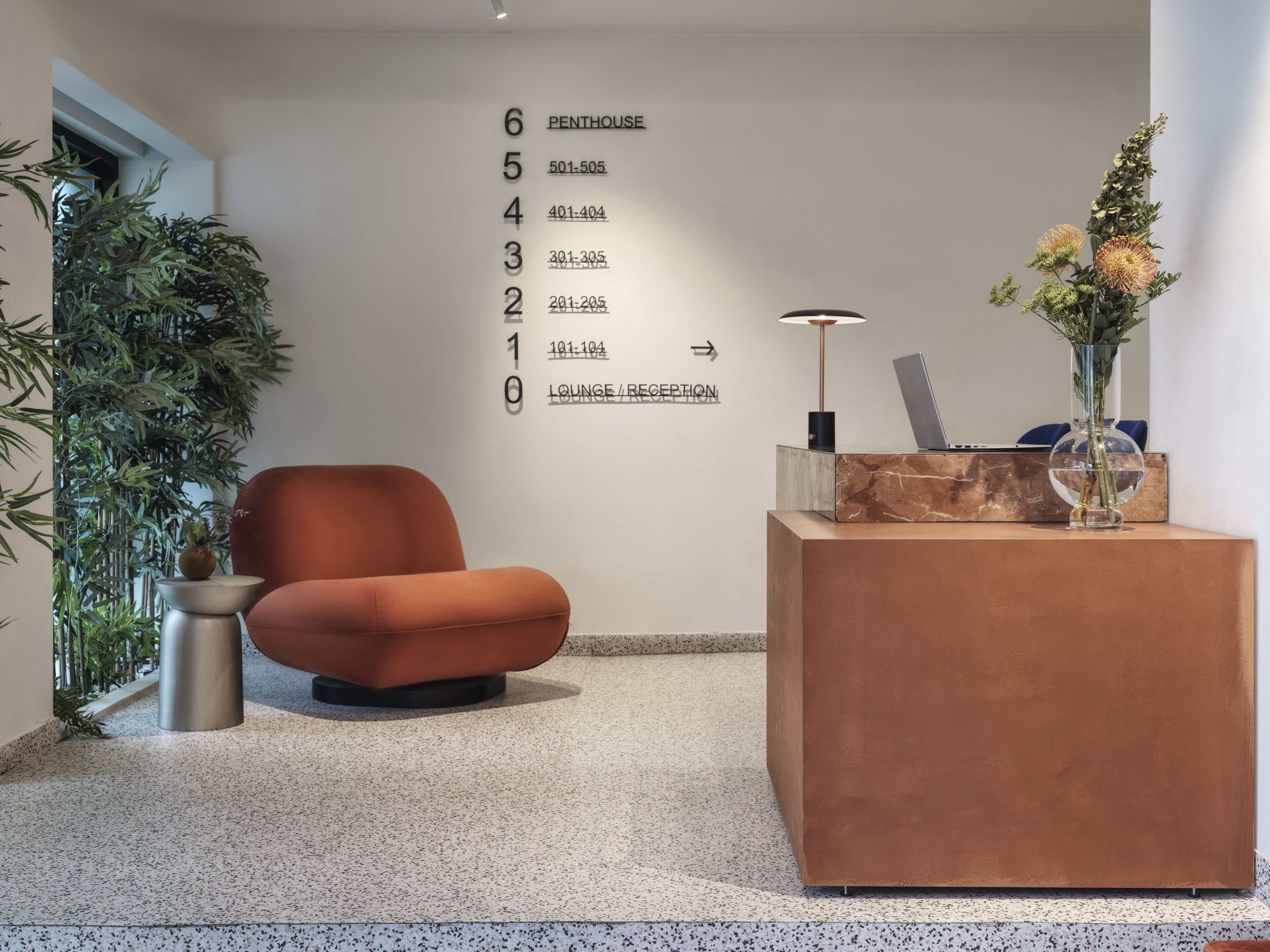 Un vestíbulo moderno con un mostrador de recepción, un área de descanso y una planta grande en maceta.