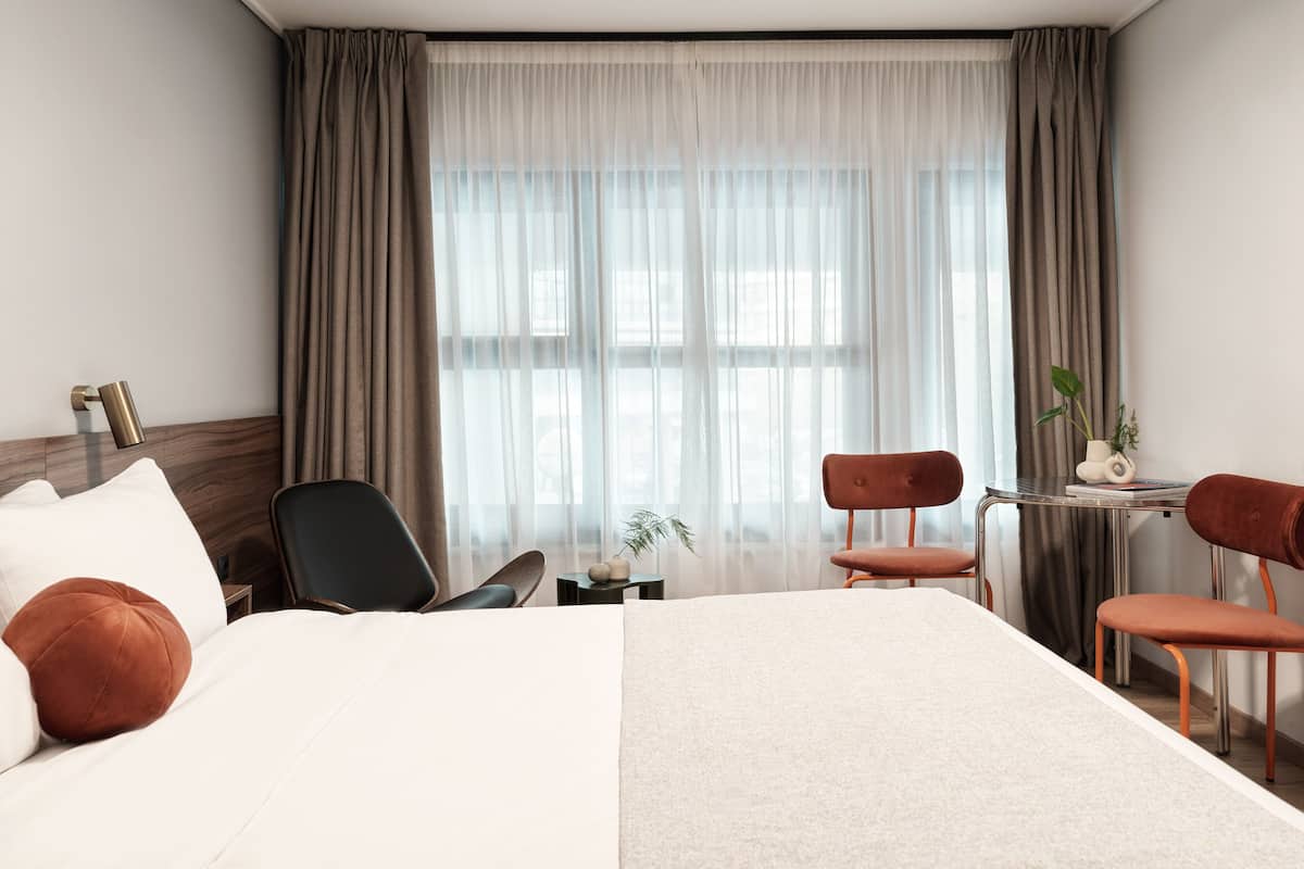 A hotel room with a large bed, two chairs, a small table, a lamp, and a window with curtains.