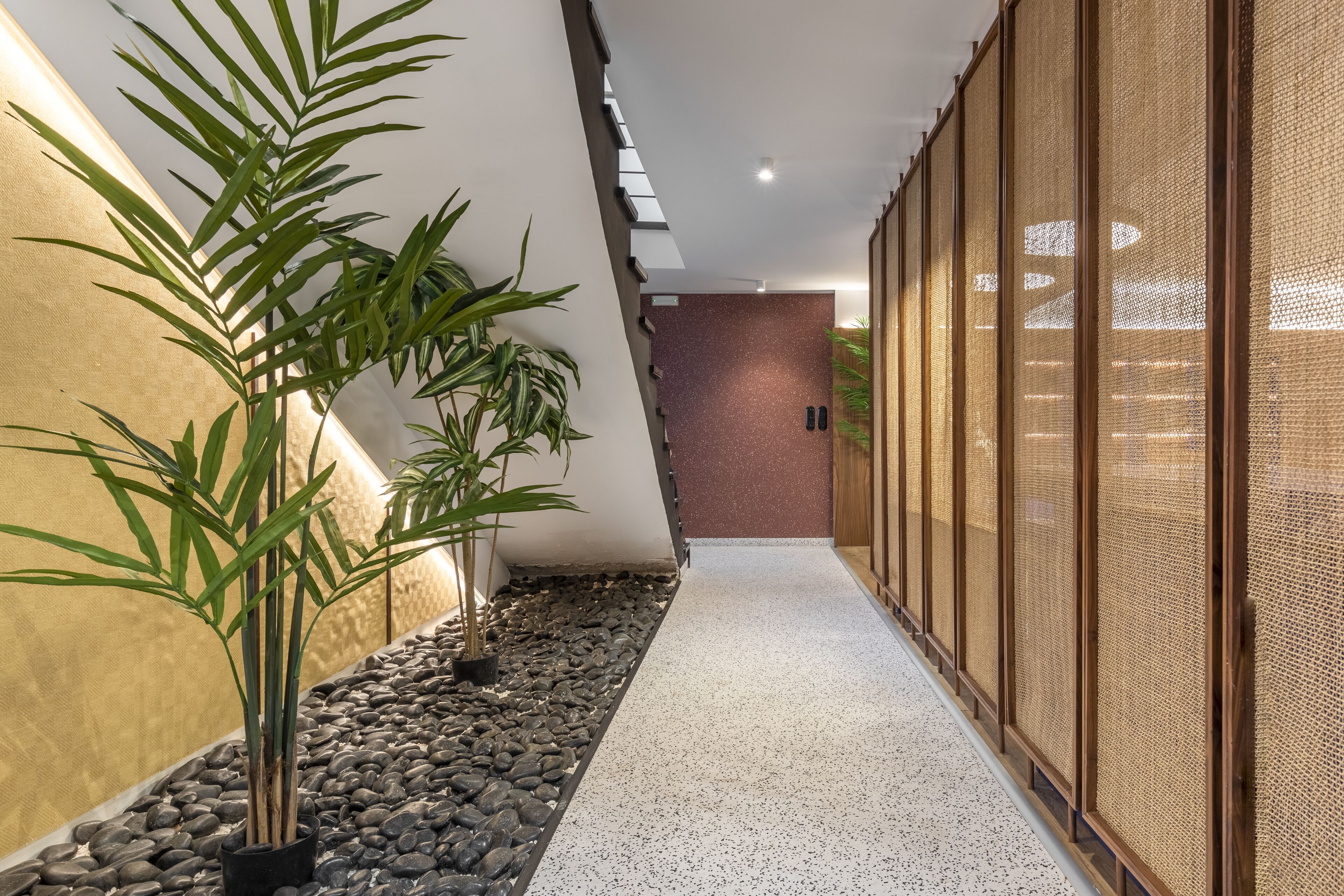 A corridor with a pebble path, bamboo plants, and a wooden screen wall.