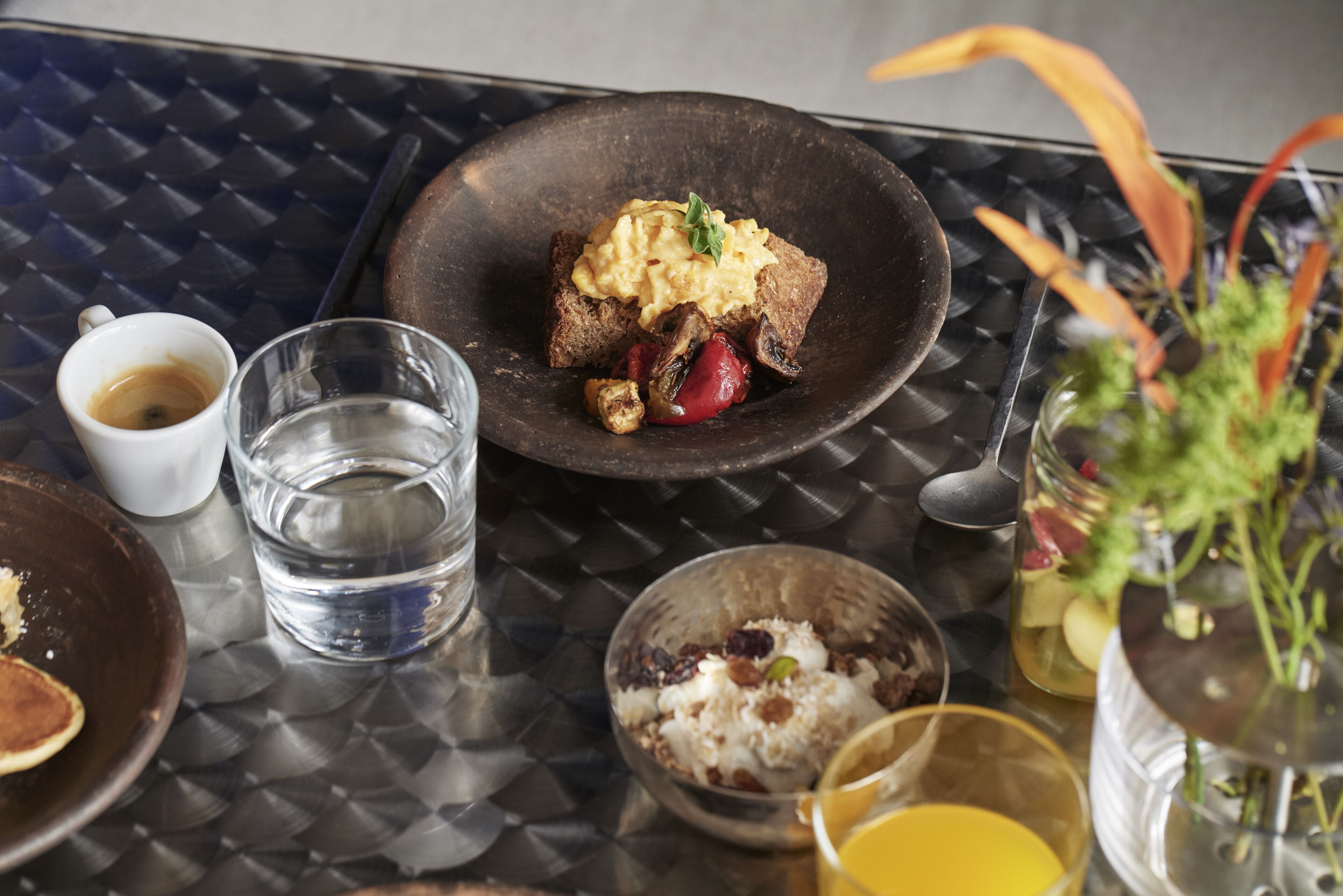 Une table à manger où l’on trouve une variété de plats, notamment des œufs brouillés sur des toasts, un bol de riz et un verre de jus d’orange.